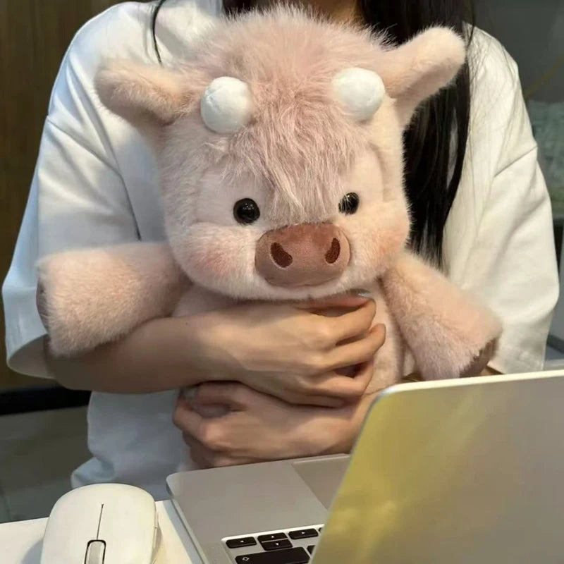 Person holding a pink plush cow toy in front of a laptop